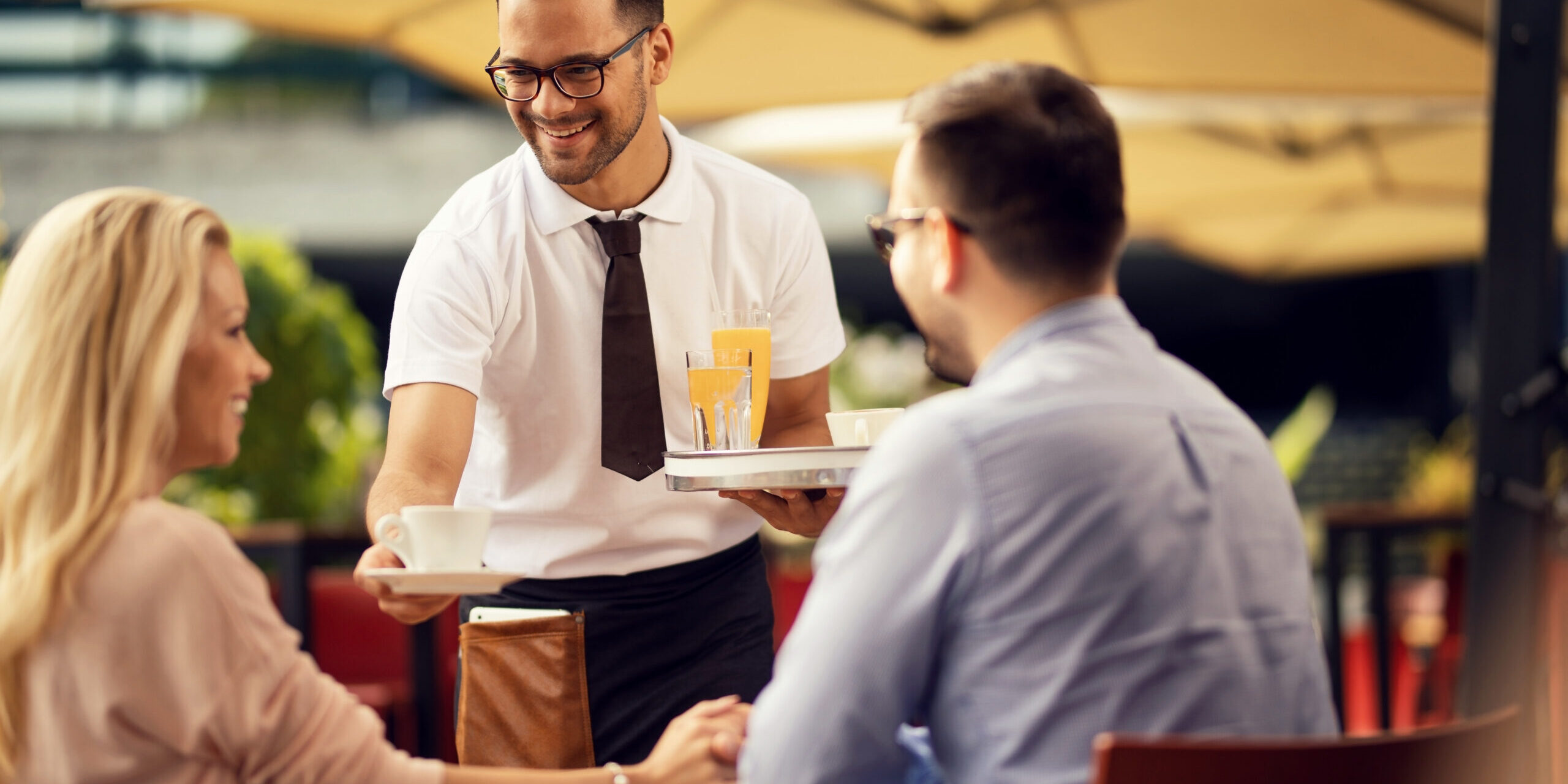 Happy waiter serving guests and giving them coffee in a cafe.