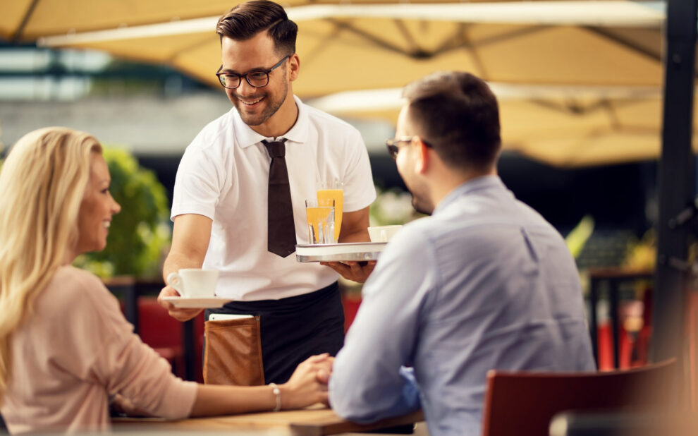 Happy waiter serving guests and giving them coffee in a cafe.