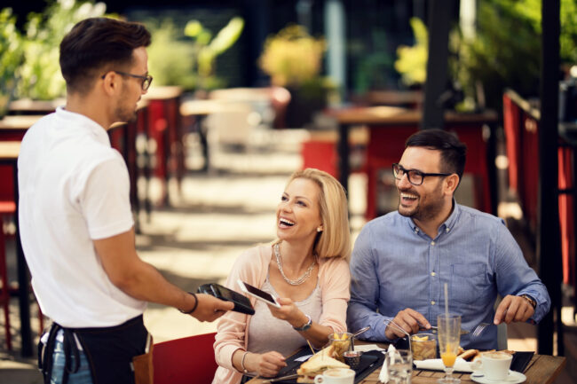 Waiter taking a smart phone payment from his guests in a restaurant.