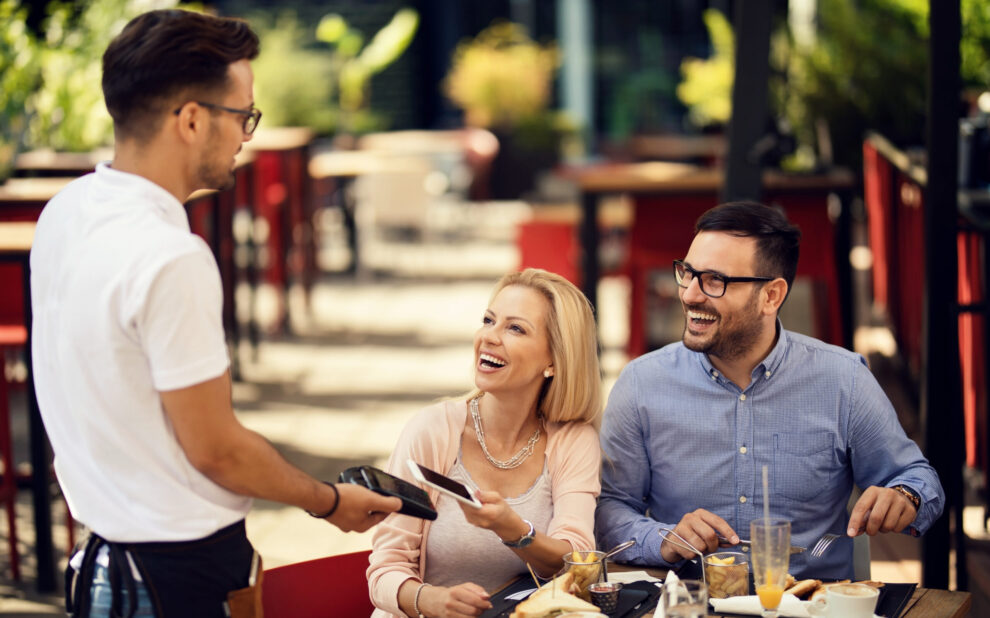 Waiter taking a smart phone payment from his guests in a restaurant.
